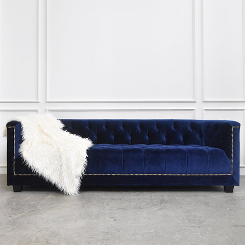 Countess II of Chesterfield sofa in navy blue with white fur throw on edge of sofa. 